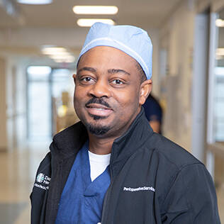 Smiling health care provider dressed in scrubs, standing in a hospital hallway