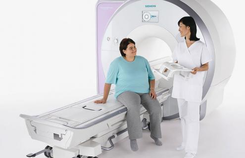 Two women - one sitting and one standing - near a Siemens MRI machine